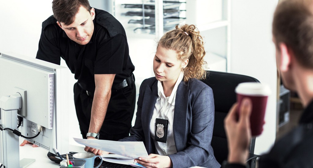 Two law enforcement officers review a paper accreditation file.