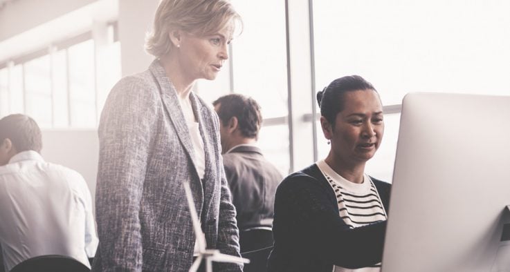 Two female employees review an SOP manual together.