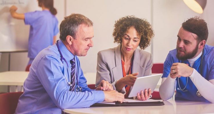 Two healthcare workers review a document on a tablet.