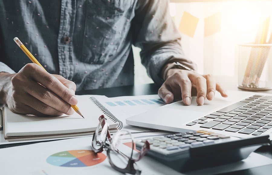 man making notes on a graph in front of laptop